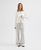 Woman wearing a white long-sleeve top and light gray pants on a white background