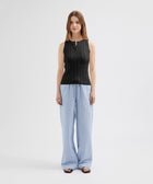 Woman wearing a black sleeveless top and light blue striped pants on a white background