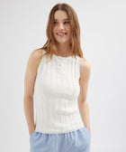 Woman wearing a white sleeveless top with a plain background