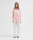 Woman wearing a pink shirt and white pants on a white background