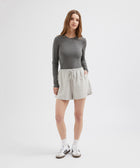 Woman wearing a gray long-sleeve top and light gray skirt on a white background